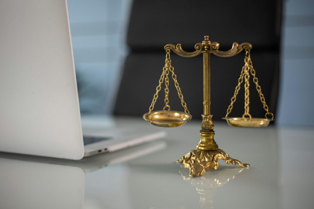 Eine goldene Justitia-Waage auf einem Schreibtisch neben einem Laptop symbolisiert Recht und Gerechtigkeit.